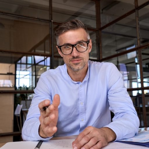 Mann mit Brille sitzt an einem Tisch mit Unterlagen